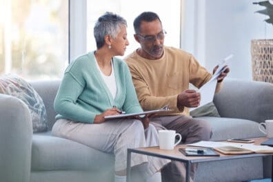 Finance, documents and senior couple on sofa with bills, paperwork and insurance checklist in home, life or asset management, Elderly black people on couch with financial, retirement or mortgage debt looking into financial planning.