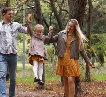 A father and mother hold up their small daughter inside a forest.