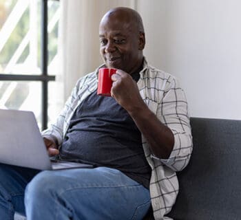 An older man drinks coffee while using the computer to easily switch his direct deposit to Lafayette Federal Credit Union