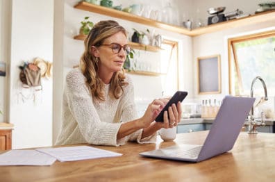 Woman with laptop and phone in home kitchen managing finances
