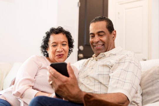 Husband and wife smile and look at pictures on their cell phone