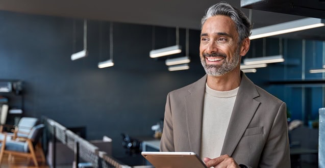 Happy mature business man ceo executive standing in office with tablet.