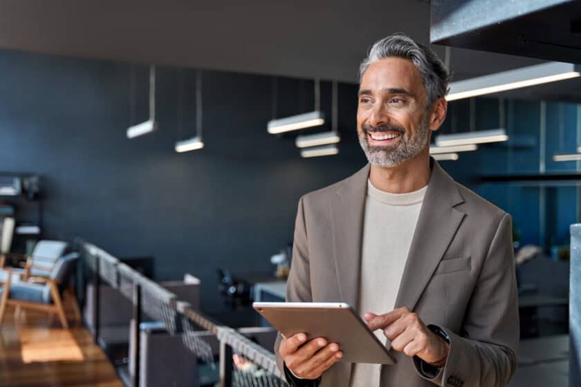 Happy mature business man ceo executive standing in office with tablet.