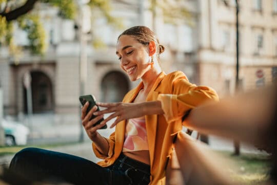 Smiling university student checks phone outdoors on sunny campus in the afternoon