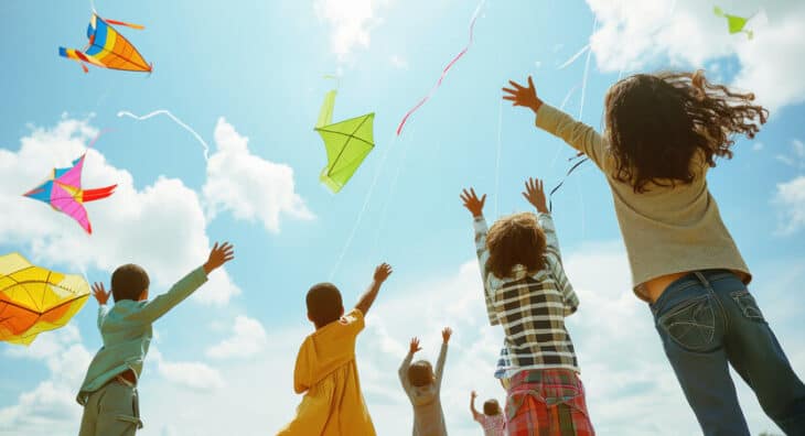 Kite flying with children outdoors on sunny day, colorful kites in sky, family enjoying summer activity at Lafayette Federal Credit Union.